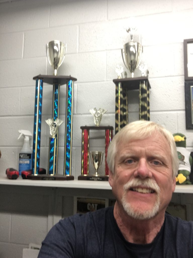 Professor Gary Phares poses in front of some of his racing trophies.