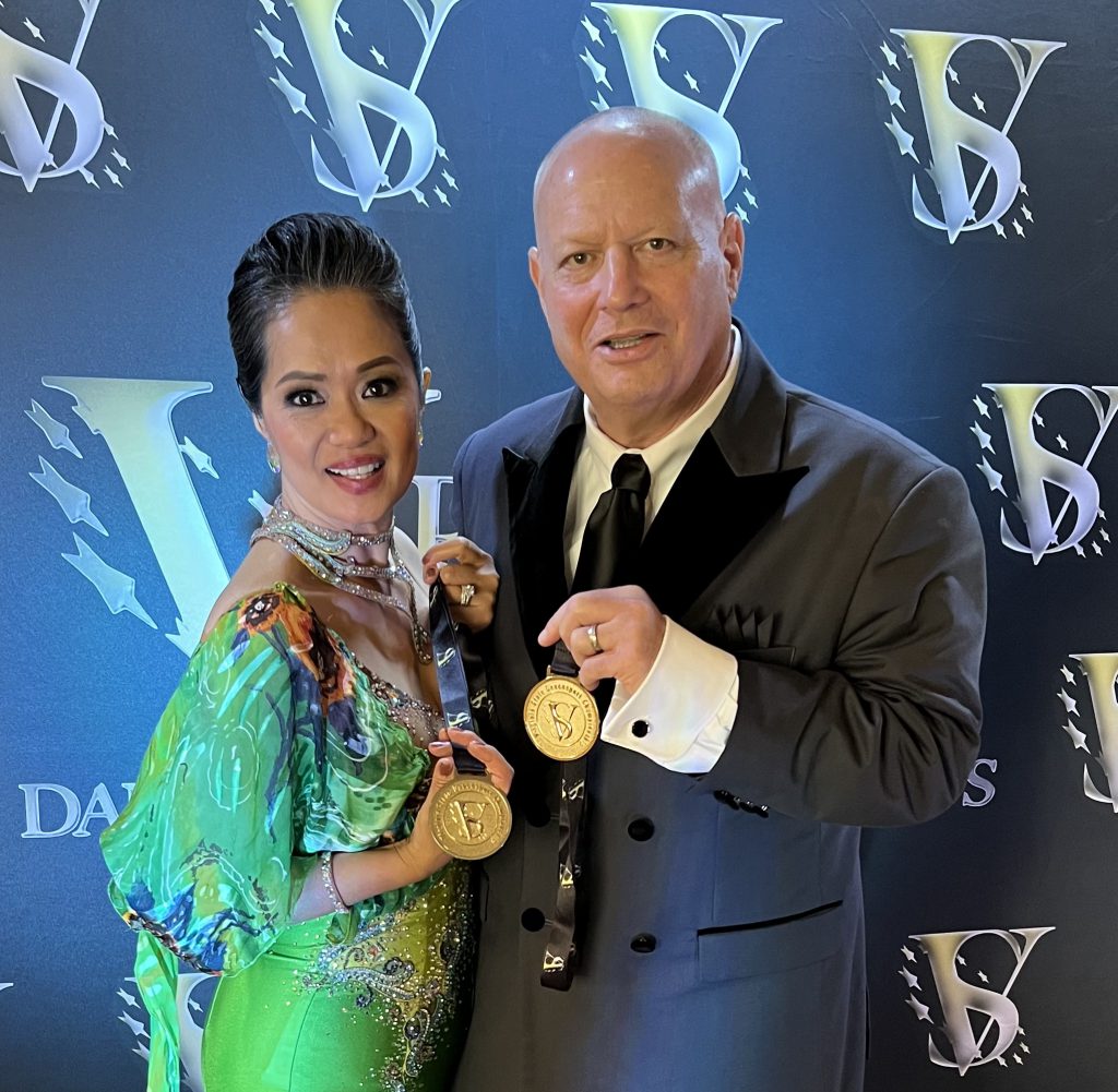 Professor Alan Golombek poses with his wife, Thuy, as they show their medals from their first-place win at the DanceSport state championship
