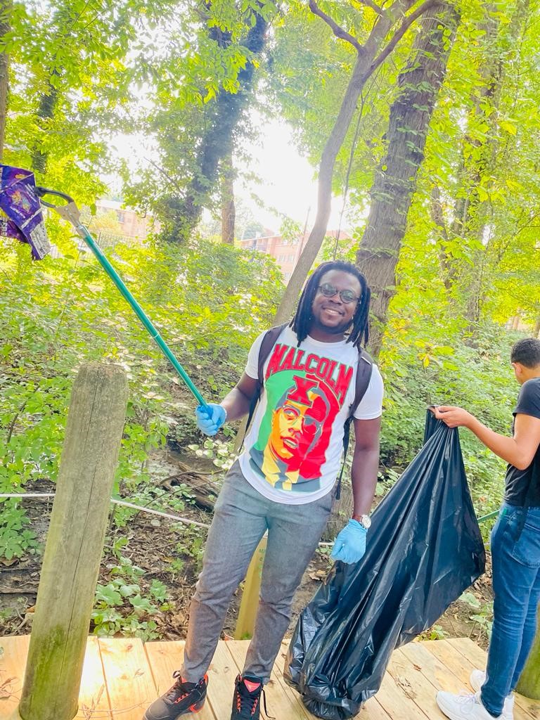 CCI student wearing colorful Malcolm X tee smiles as he collects trash from the park