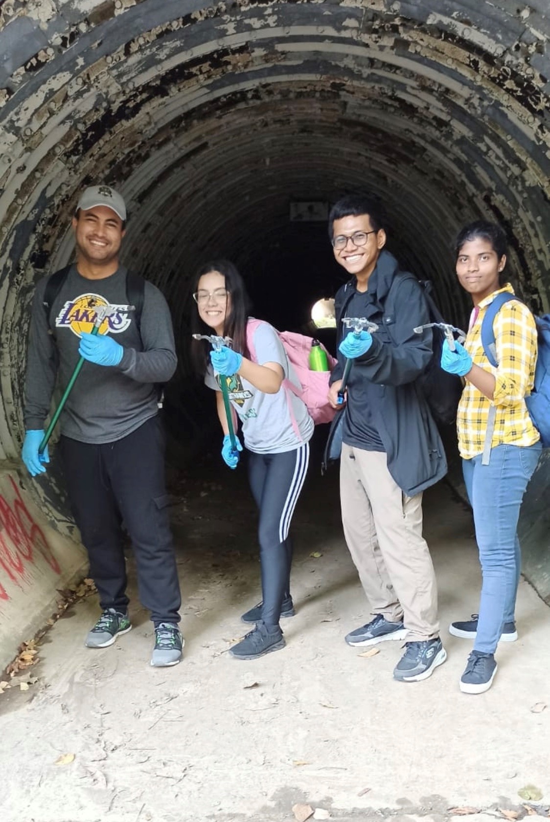 Four CCI students with their "trash grabbers" stand inside a storm drain as they collect trash for their service project.