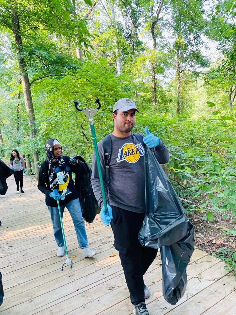CCI Student with grey baseball cap and grey LA Lakers shirt gives a thumbs up as he takes a break from collecting trash.