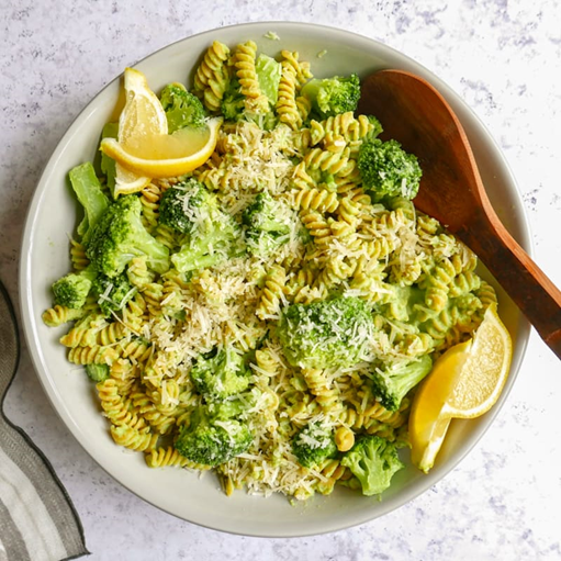 Photo of a plate with spiral rotini pasta and broccoli sauce, with broccoli, lemon wedges and topped with parmesan cheese.