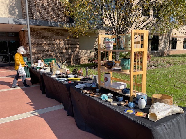 Woman in a bright yellow puffer jacket shops at the Annandale Campus pottery sale during a previous year.