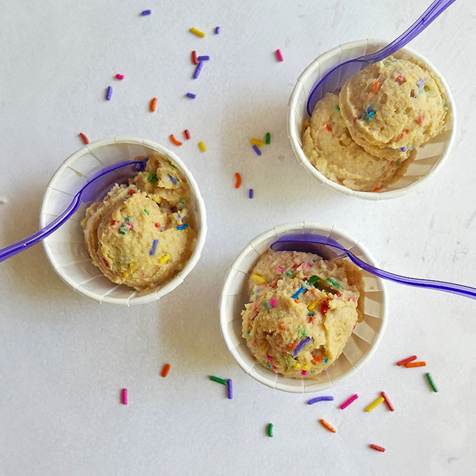 Cups of safe-to-eat cookie dough with sprinkles and little blue spoons!
