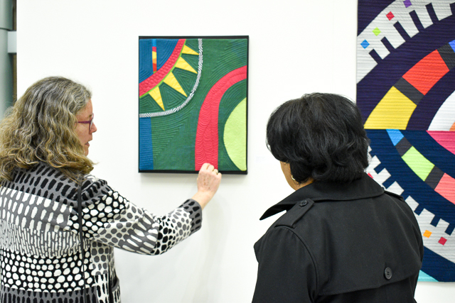 Artist and Quilter Cindy Grisdela shows the intricate detail of the stitching hidden beneath the design of her quilt to a visitor of the exhibit.