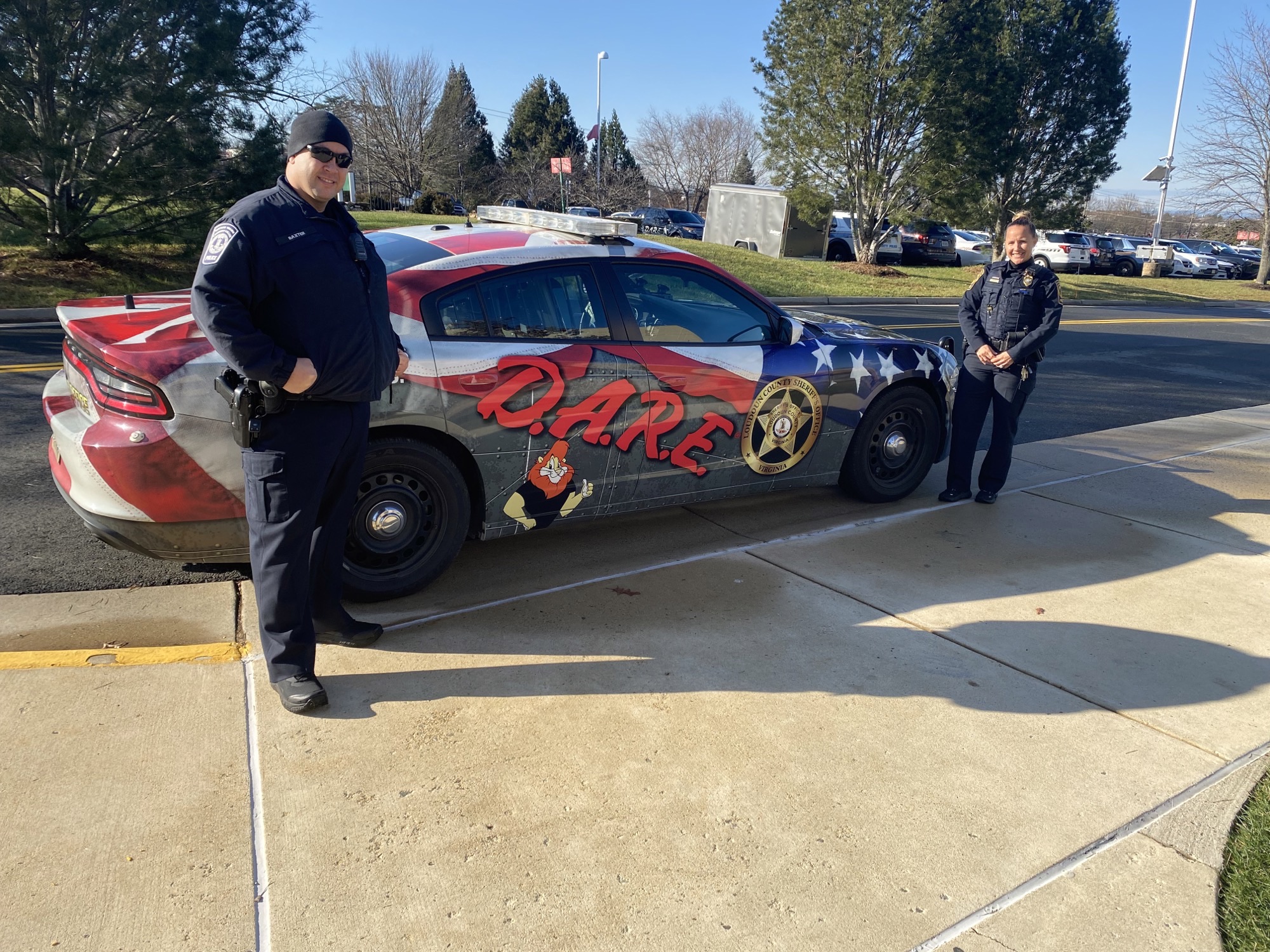 Two uniformed officers stand next to the DARE vehicle