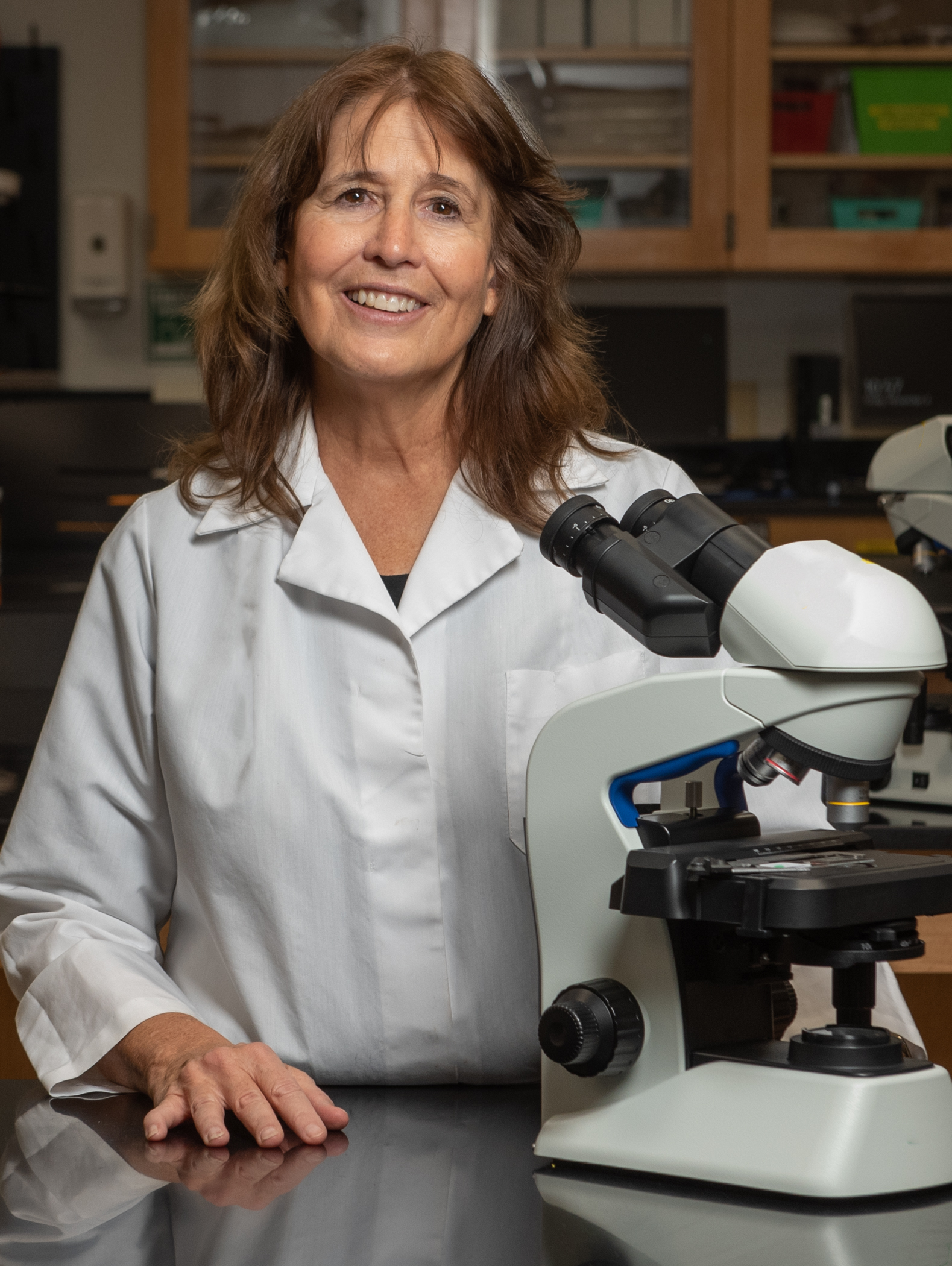 Caporale, wearing a white lab coat, stands beside a microscope in one of NOVA's science labs.