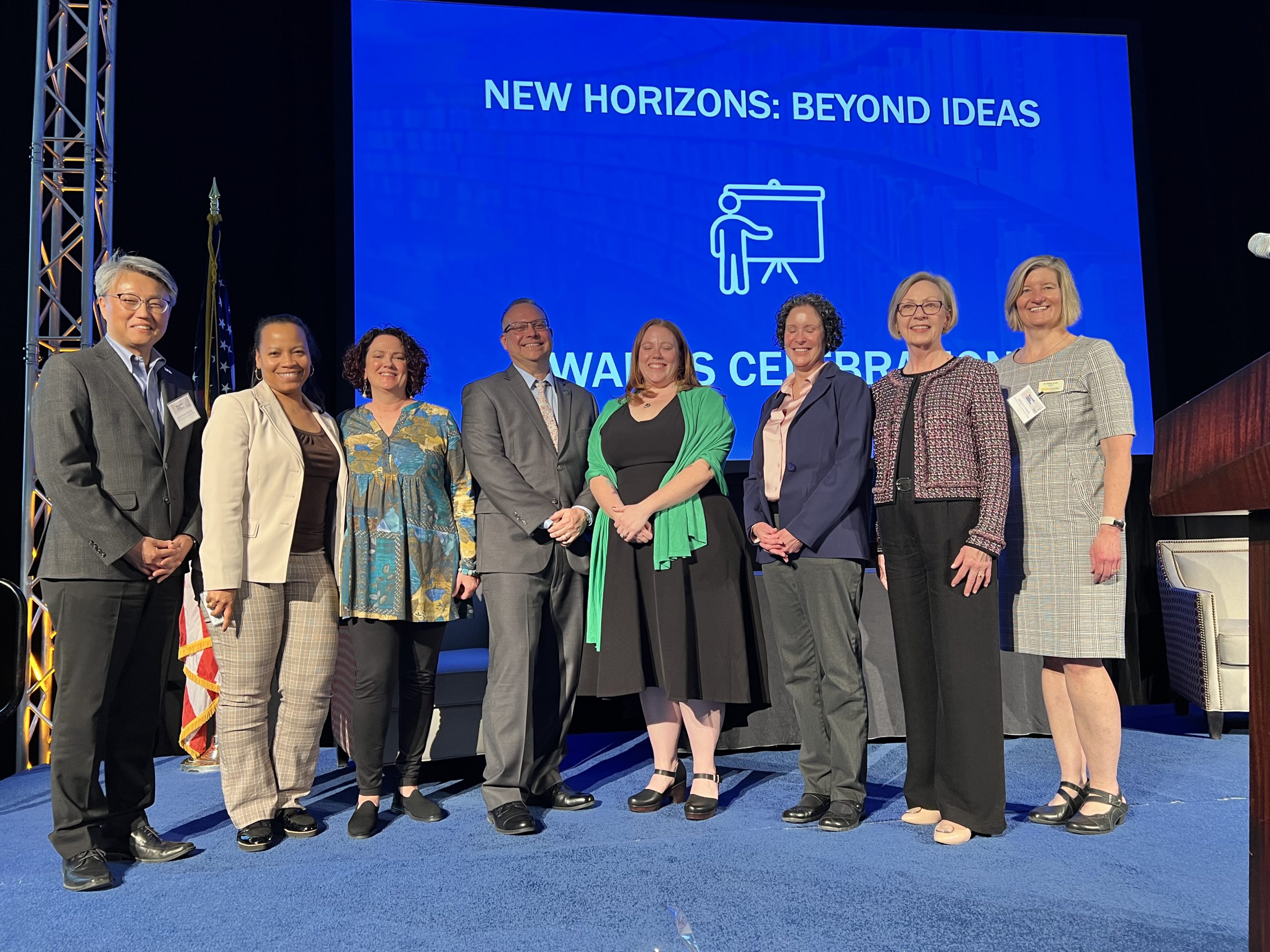 NOVA participants line up before a blue screen with a slide saying "New Horizons: Beyond Ideas Awards Ceremony. Left to Right: Dr. Eun-Woo Chang, CAO and VP of Academic Affairs; Barbara Hopkins, AVP of Academic Affairs; Alicia Tucker; Paul Fitzgerald; Cheri Spiegel; Cynthia Hatch; Dr. Sharon Morrissey , Acting VCCS Chancellor; Dr. Molly Lynch, Provost, Manassas Campus
