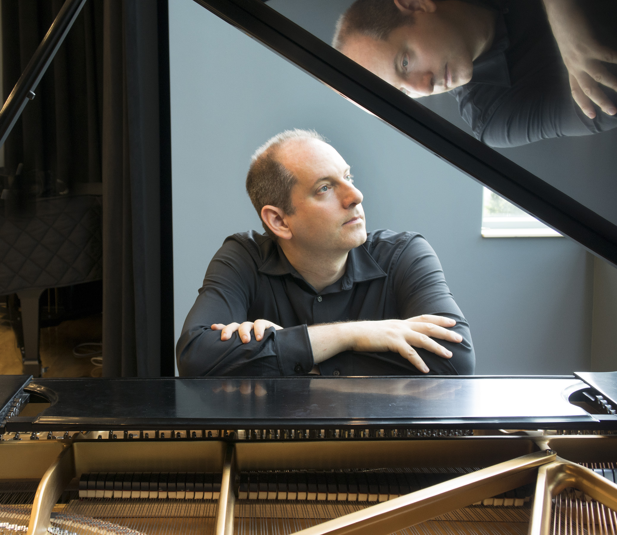 Jonathan Kolm sits at grand piano, arms crossed above the keys, looking off to the side.,
