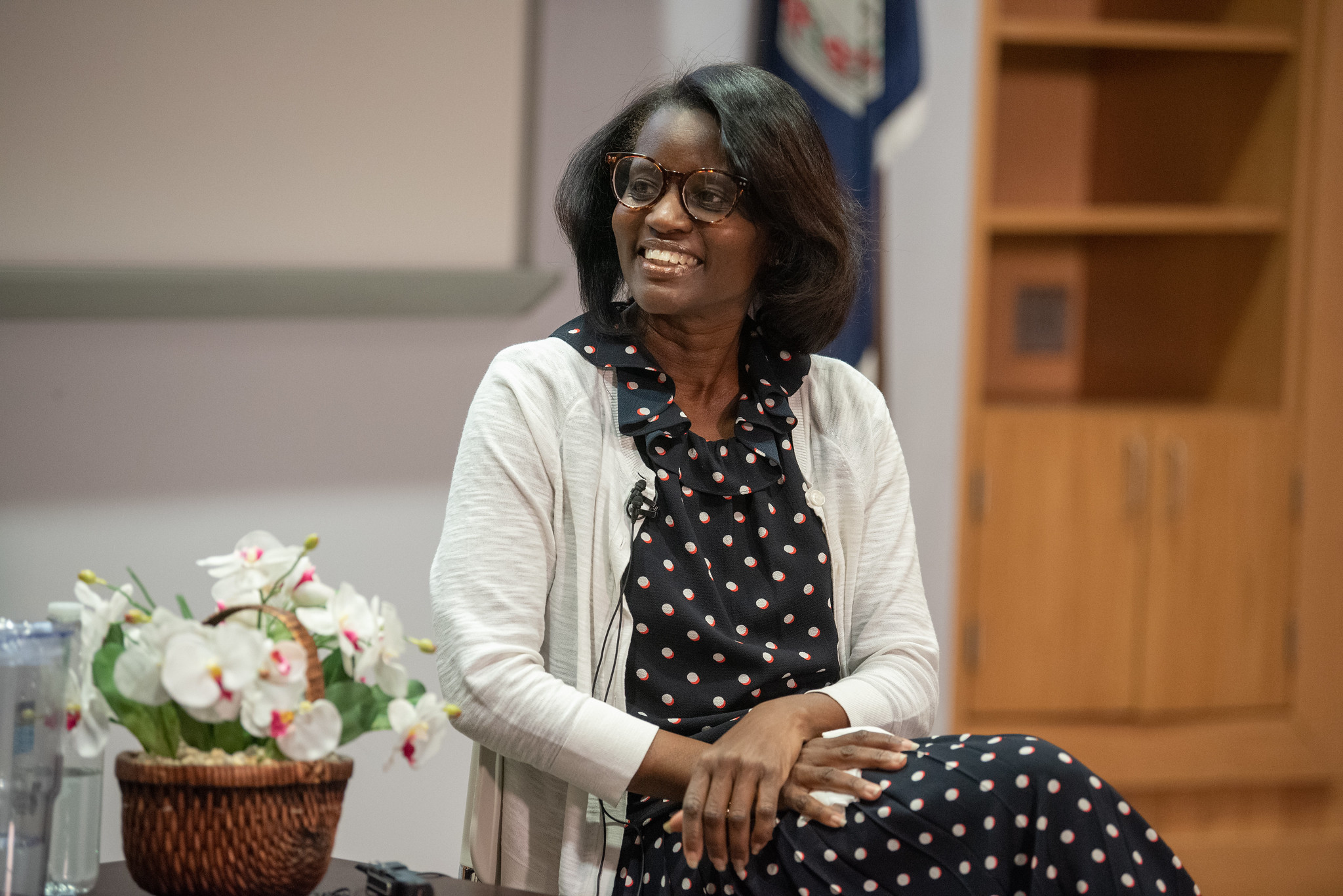 Kim Haas, wearing a black and white polka dot dress and a white sweater sits next to a basket of begonias at the event.