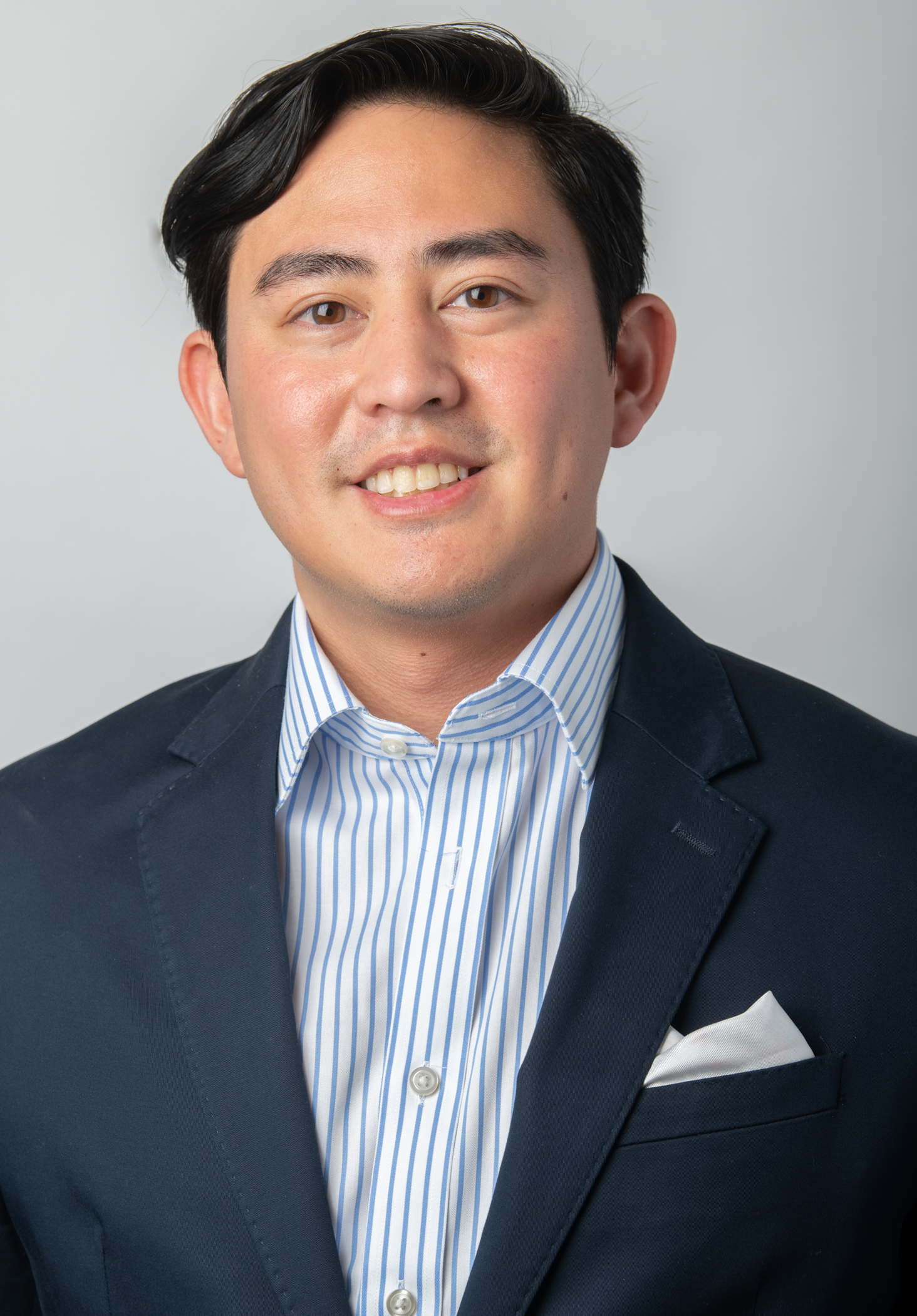 Arthur Tamayo smiles, wearing a navy blue blazer over a light blue button down oxford shirt.