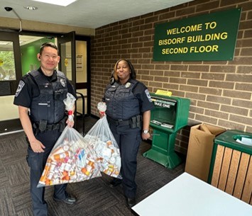 Officer Jeffrey Liu and Officer Lashana Combs hold large garbage bags full of medicine bottles.