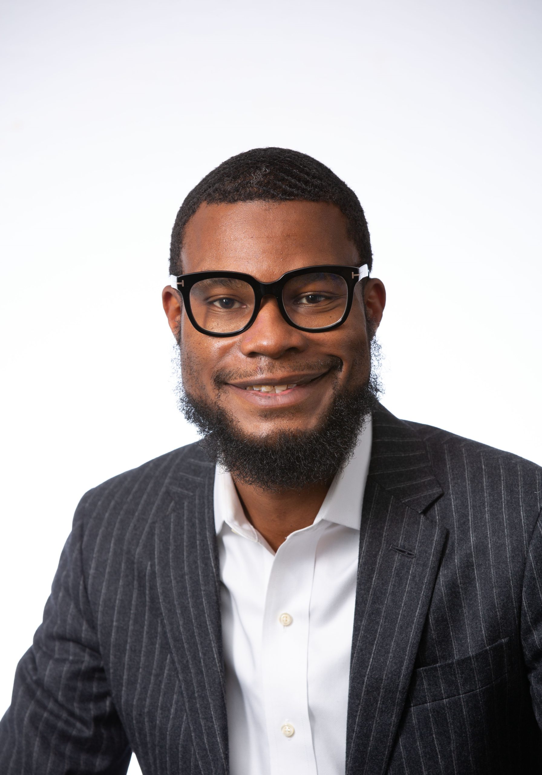 Professional headshot of Kevin Baisden wearing horn-rimmed glasses, a white oxford shirt and a black, pin-striped blazer