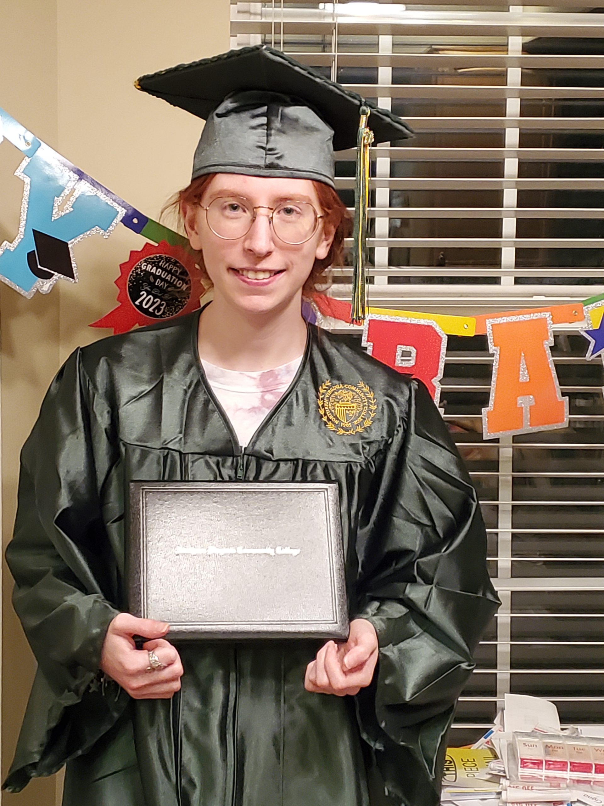 Happy graduate Nicole Goldman, wearing her NOVA graduation cap and gown and holding her diploma at a family party to celebrate her big achievement
