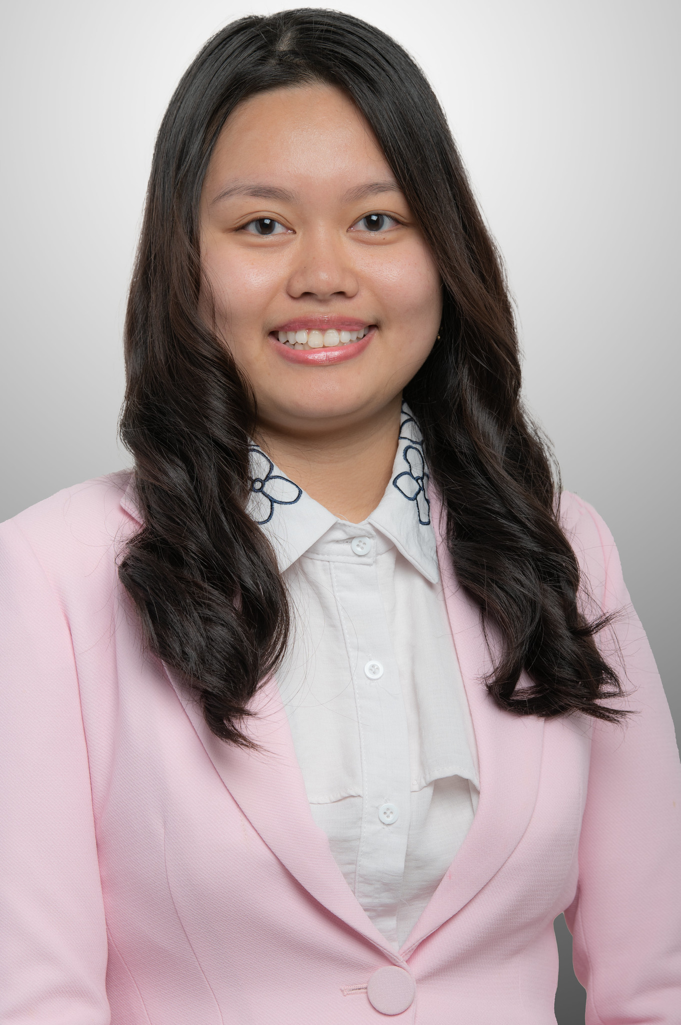 Smiling portrait of Ollie Vo, wearing a light pink suit jacket and white button down blouse