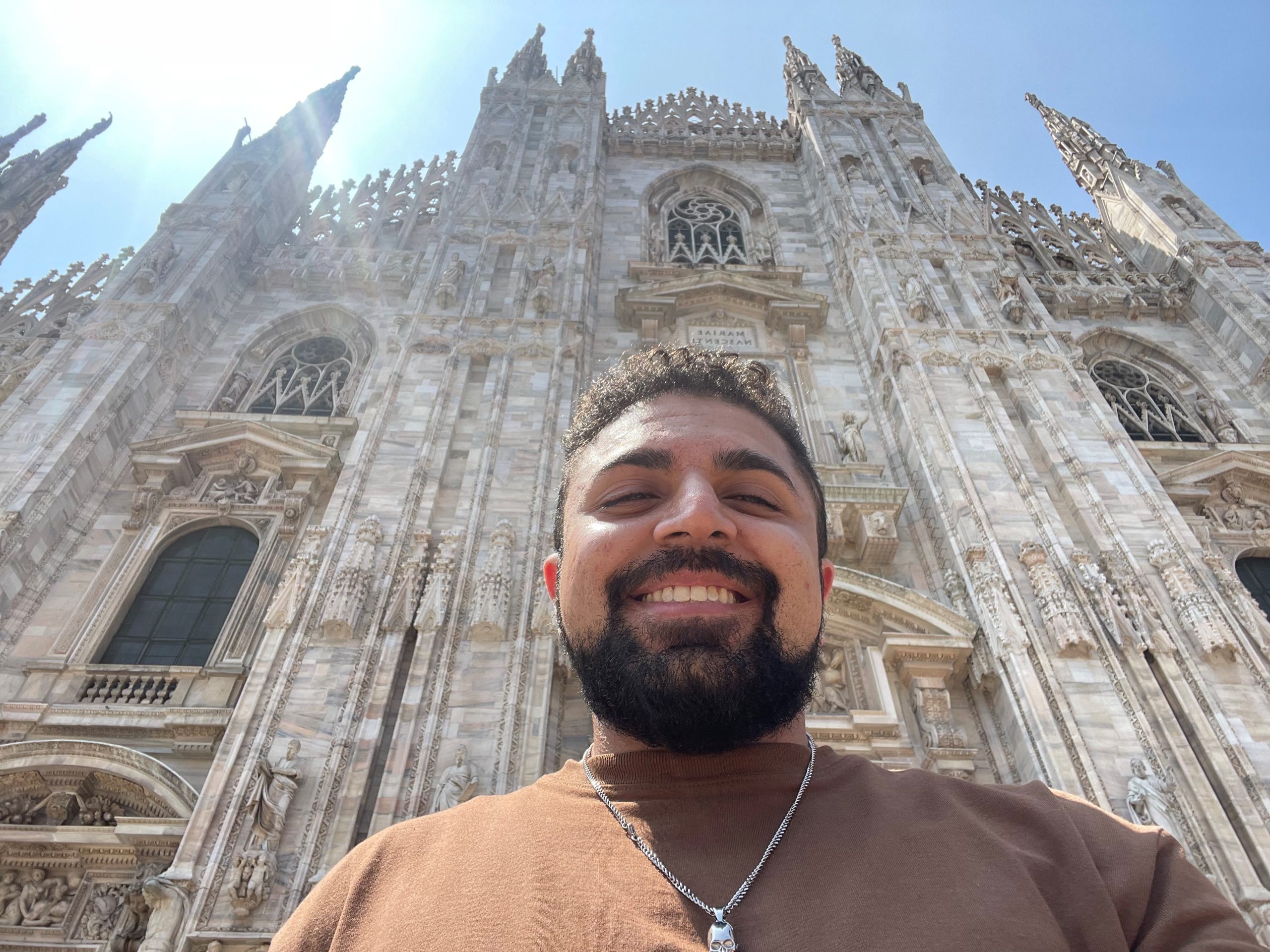 Limar Aryan smiles for a selfie against the backdrop of a beautiful Italian cathedral on a bright, sunny day in Italy.
