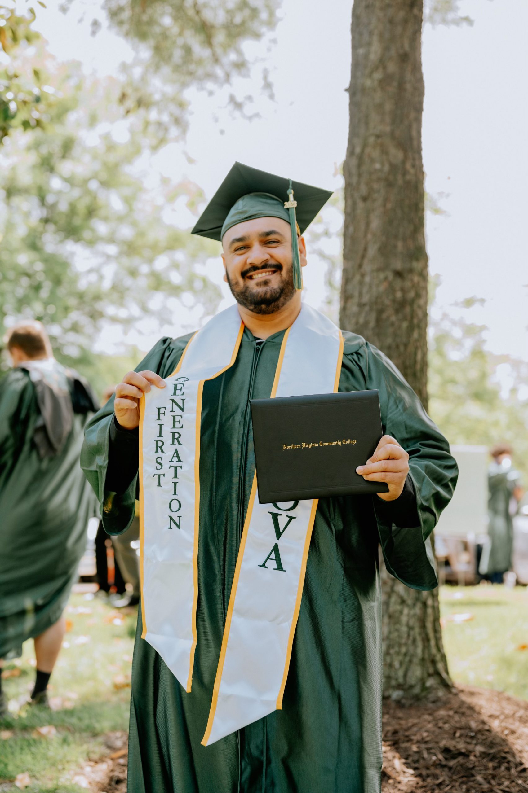 Proud spring 2023 graduate Anthony DeJesus beams in his graduation regalia with a sash that says "First Generation"