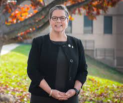 President Anne M. Kress stands outside the Mark Warner Student Services Building on the Annandale Campus on a beautiful fall day with a tree's changing leaves behind her.