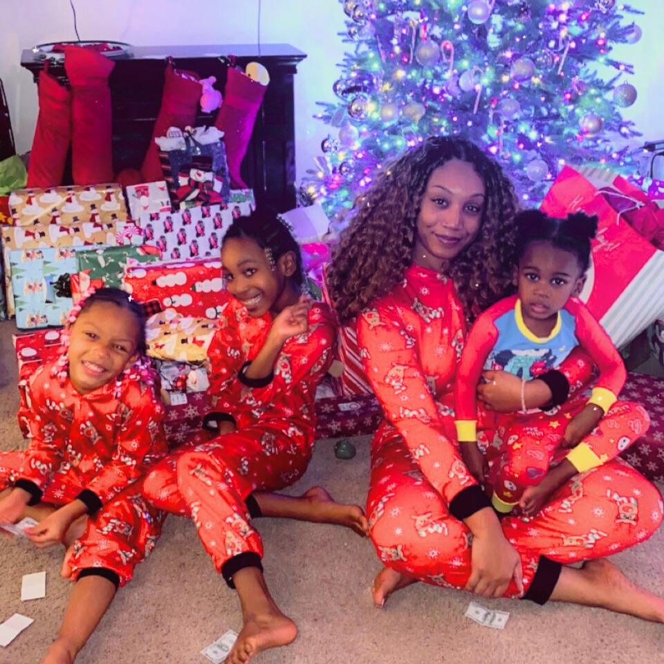 Solange and her three children, dressed in matching red character pajamas sit amongst their Christmas presents in front of a tinsel tree.
