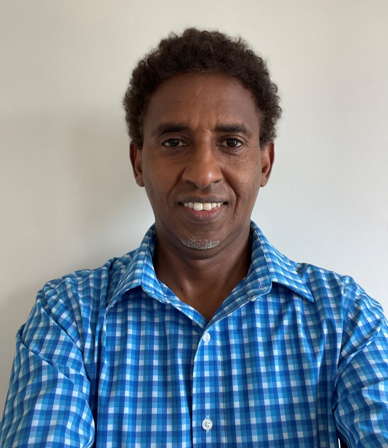 Mohamed Del, wearing a blue checkered shirt smiles for a selfie