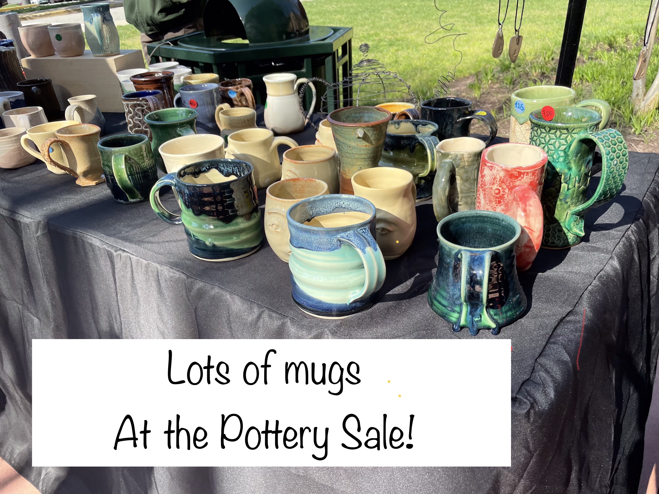 Photograph of a table from previous year laden with mugs of every color, size and style. White banner with black type: Lots of mugs at the Pottery Sale!