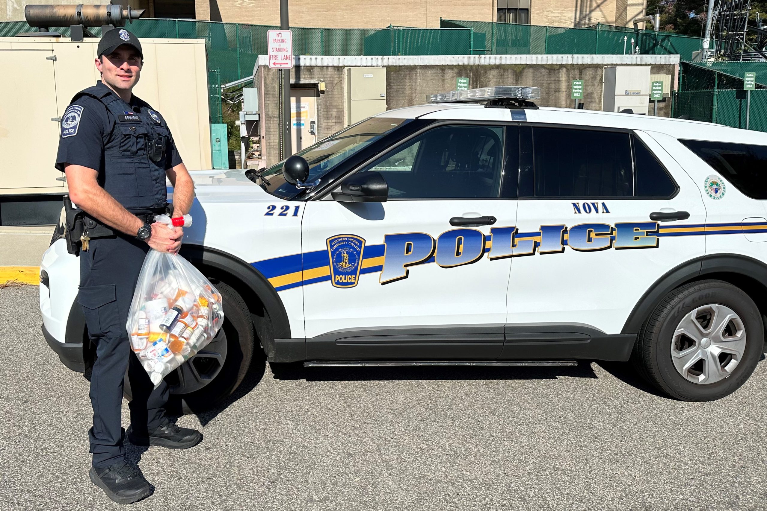 Officer Samuel Souligne holds the bag of collected prescription drugs while standing in front of a NOVA Police vehicle..