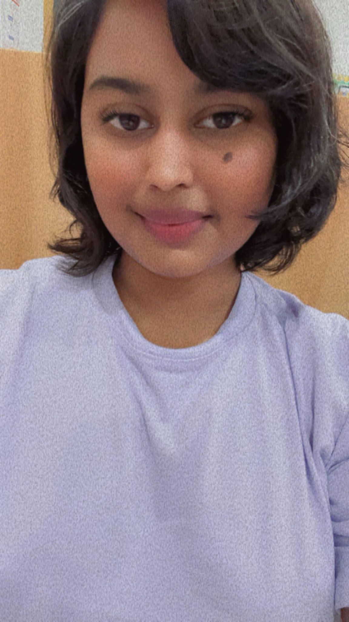NOVA nursing student Menuka Puri, with chin-length dark hair and wearing a light purple shirt, takes a selfie in a classroom.