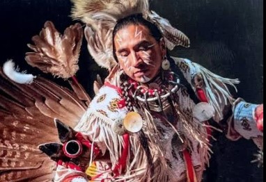 Dressed in full regalia and facepaint, photo of Yazzie in the midst of a cultural dance