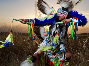 Yazzie, dressed in full regalia holds a pose in a field at sunset