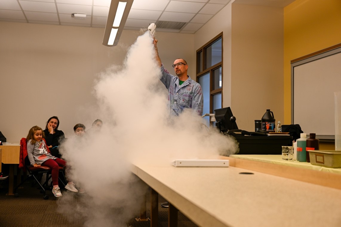 Dean Mike Davis looks up as he performs his Science Stunt Show to an enthralled audience. He holds a bottle over his head as steam blasts out of it.
