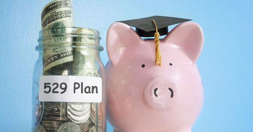 Photo. Blue background with glass jar filled with coins and $20 bills. Jar labeled "529 Plan." Pink piggy bank wearing a graduation cap and tassel. 