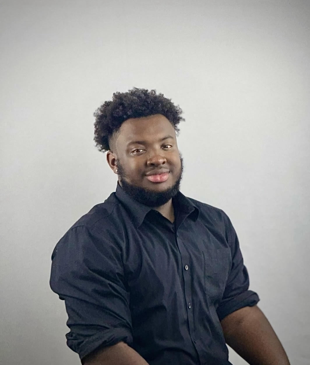 NOVA Nighthawk Jamar Pride, wearing a dark button-down shirt, smiles for the camera against a gray background.