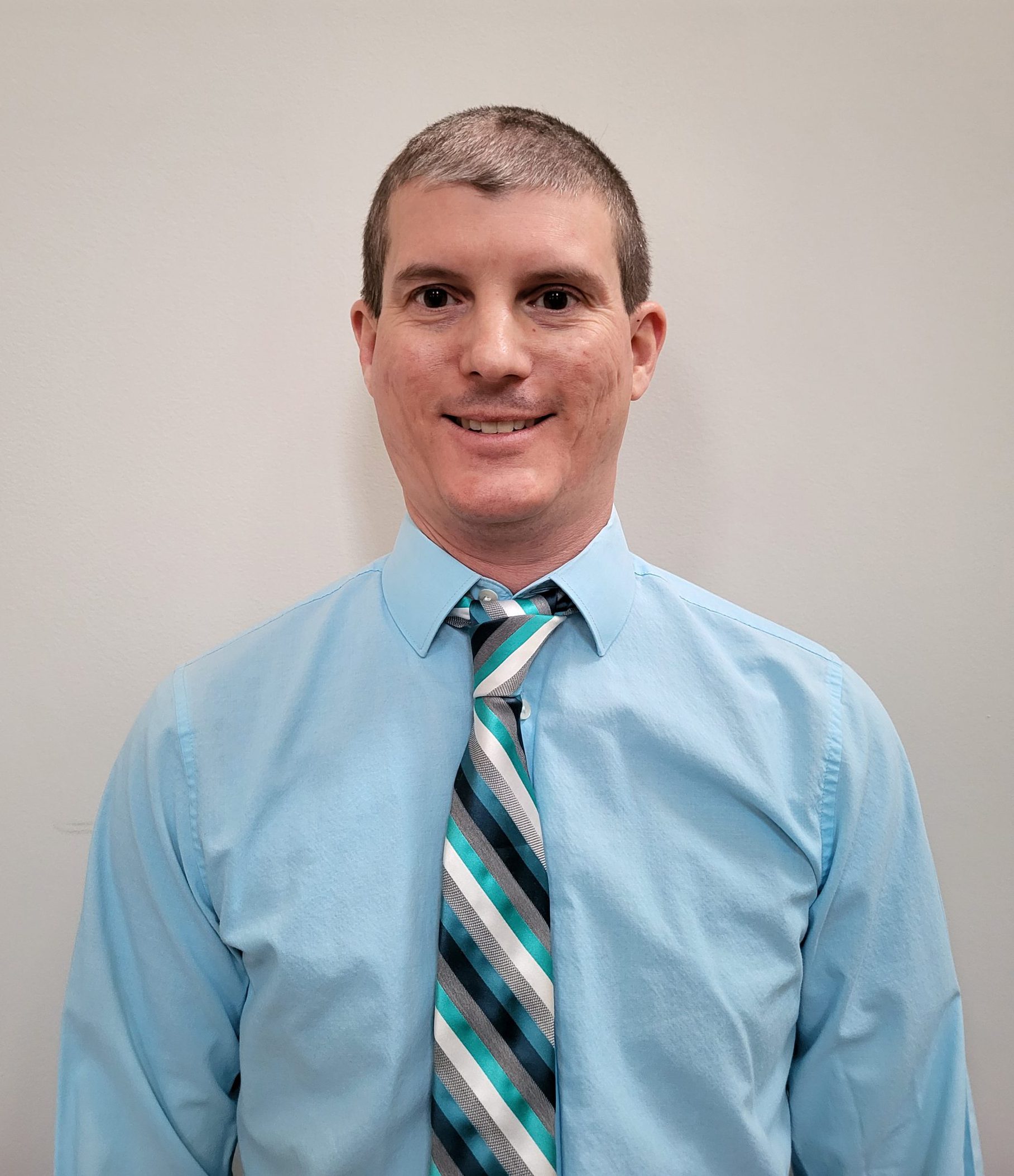 NOVA's new Office of Student Rights and Responsibilities Director Matthew Coats, wearing a light blue Oxford shirt and a blue- and white-striped tie, smiles for the camera.