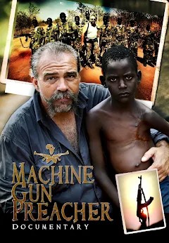 Sam Childers, known as the Machine Gun Preacher is pictured with his arm around a small boy from Sudan with a large scar on his chest. A photo in the background shows a line of child soldiers with the leader. 