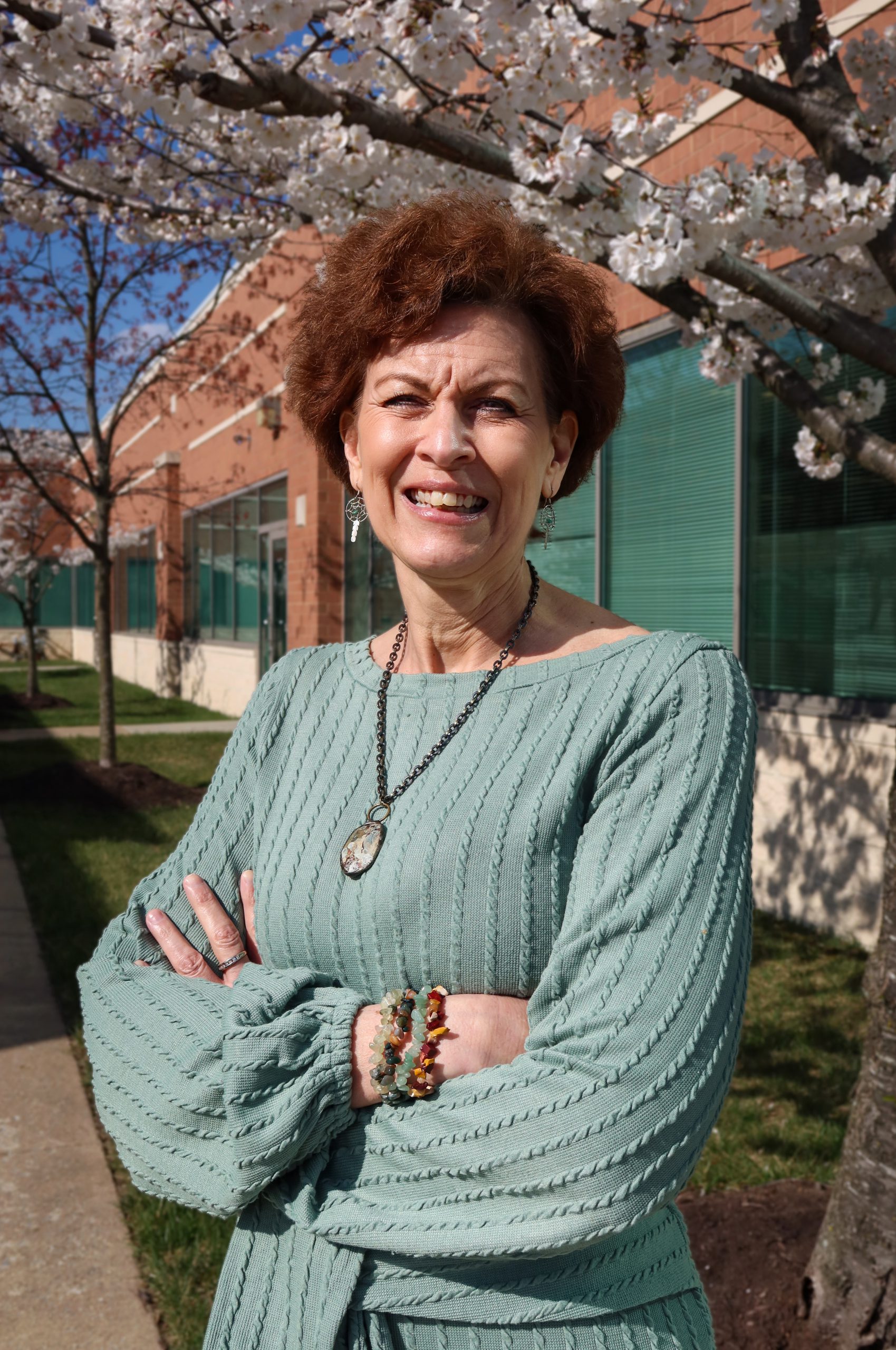 Sara Collins, wearing a seafoam green dress, poses outside on a sunny spring day amidst Pender's beautiful cherry blossoms