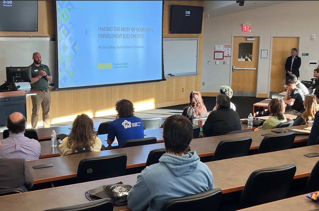 Photograph of dual enrollment students and their families attending a showcase event on the Annandale Campus. Event attendees view a screen at the front of classroom CA-302 in the Student Services Building. The PowerPoint slide displayed says, "Making the Most of Your Dual Enrollment Credits."