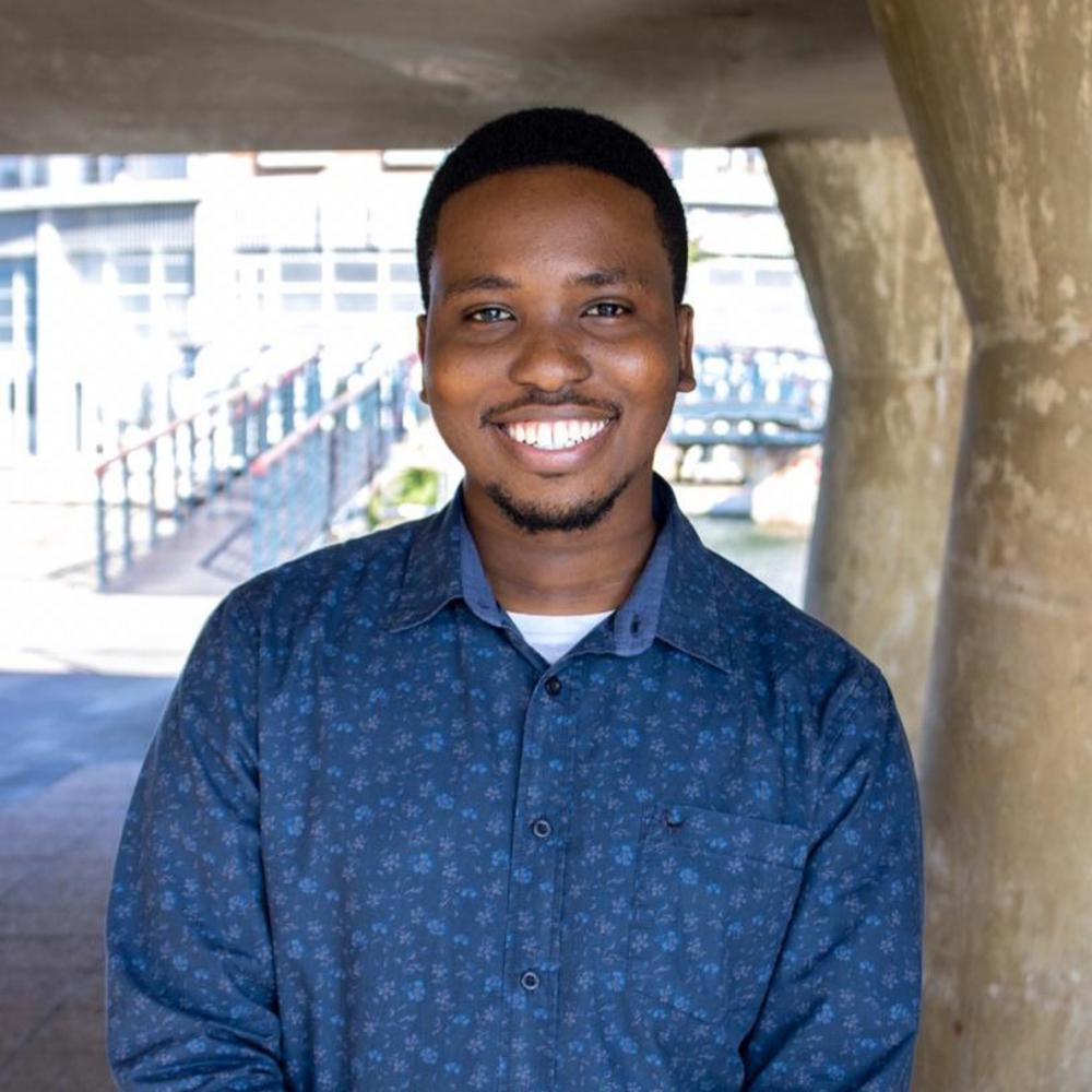 Former NOVA and CCI student Gomolemo Mohapi, who now works for Microsoft, smiles for the camera while wearing a long-sleeved button-down shirt in blue.
