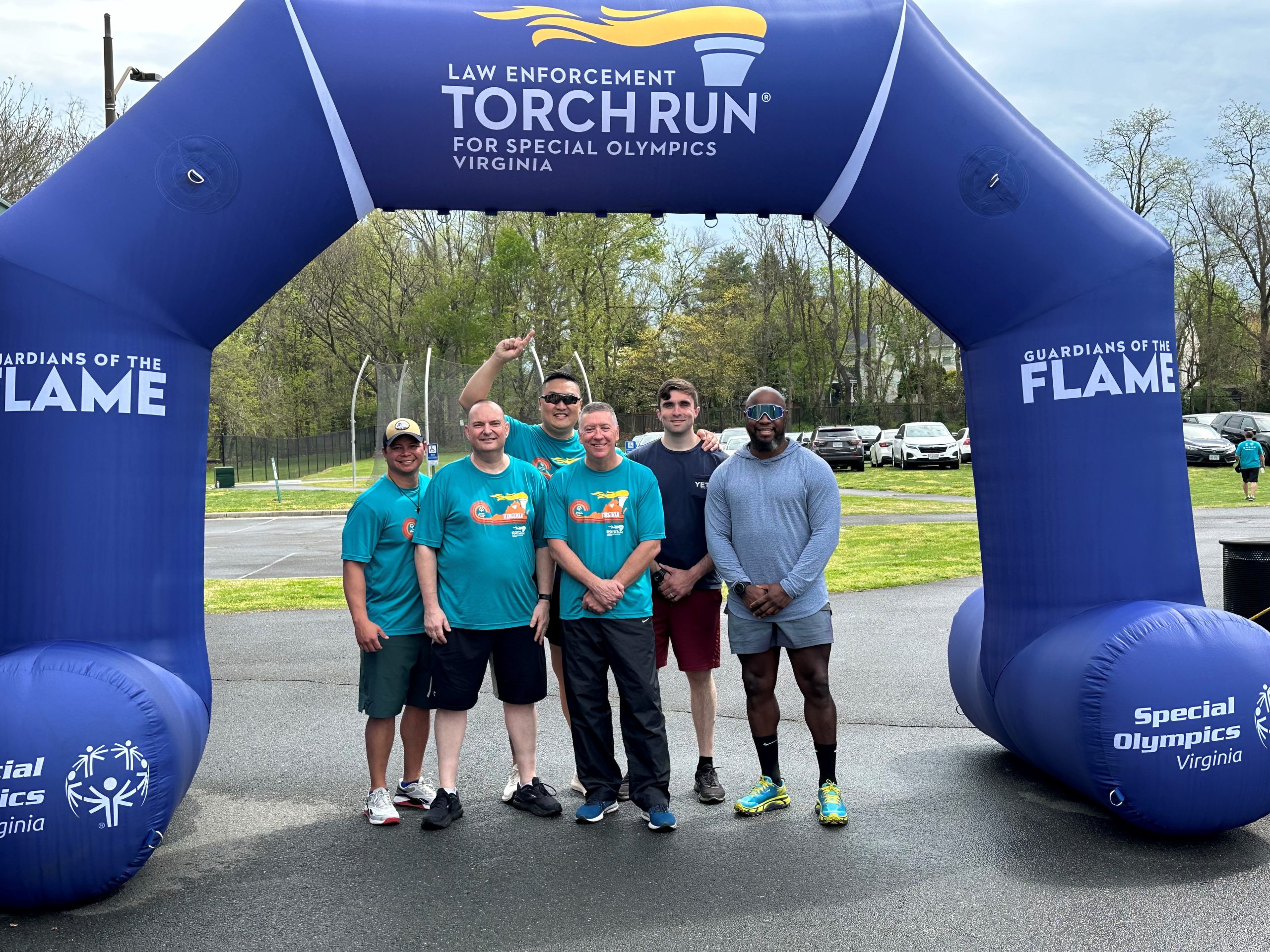 NOVA PD runners line up beneath an inflatable blue "finish line" emblazoned with the words, Guaridans of the Flame, Special Olympics and Law Enforcement Torch Run for Special Olympics Virginia. From left to right in the photo: Officer Mark Achacoso, Lieutenant Matthew Borders, Lieutenant Tony Ong, Chief, William J. Jacoby, Sergeant Samuel Souligne, and Officer Kevin Fuentes.
