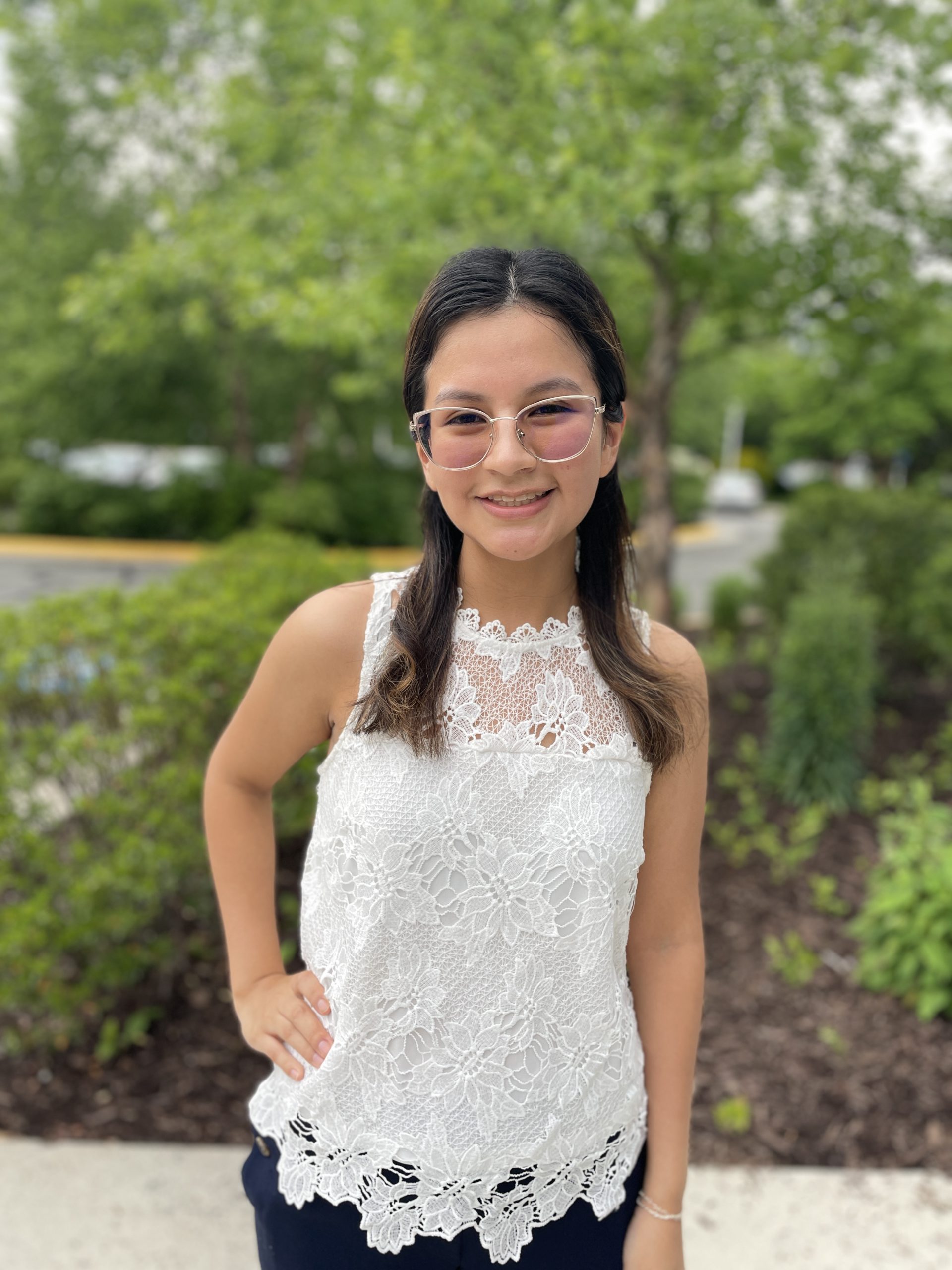 Jack Kent Cooke Foundation Undergraduate Transfer Scholarship Finalist Catherine Ercilla smiles for the camera outside the Brault building on NOVA's Annandale Campus. She wears glasses, dark pants, and a white lace blouse.