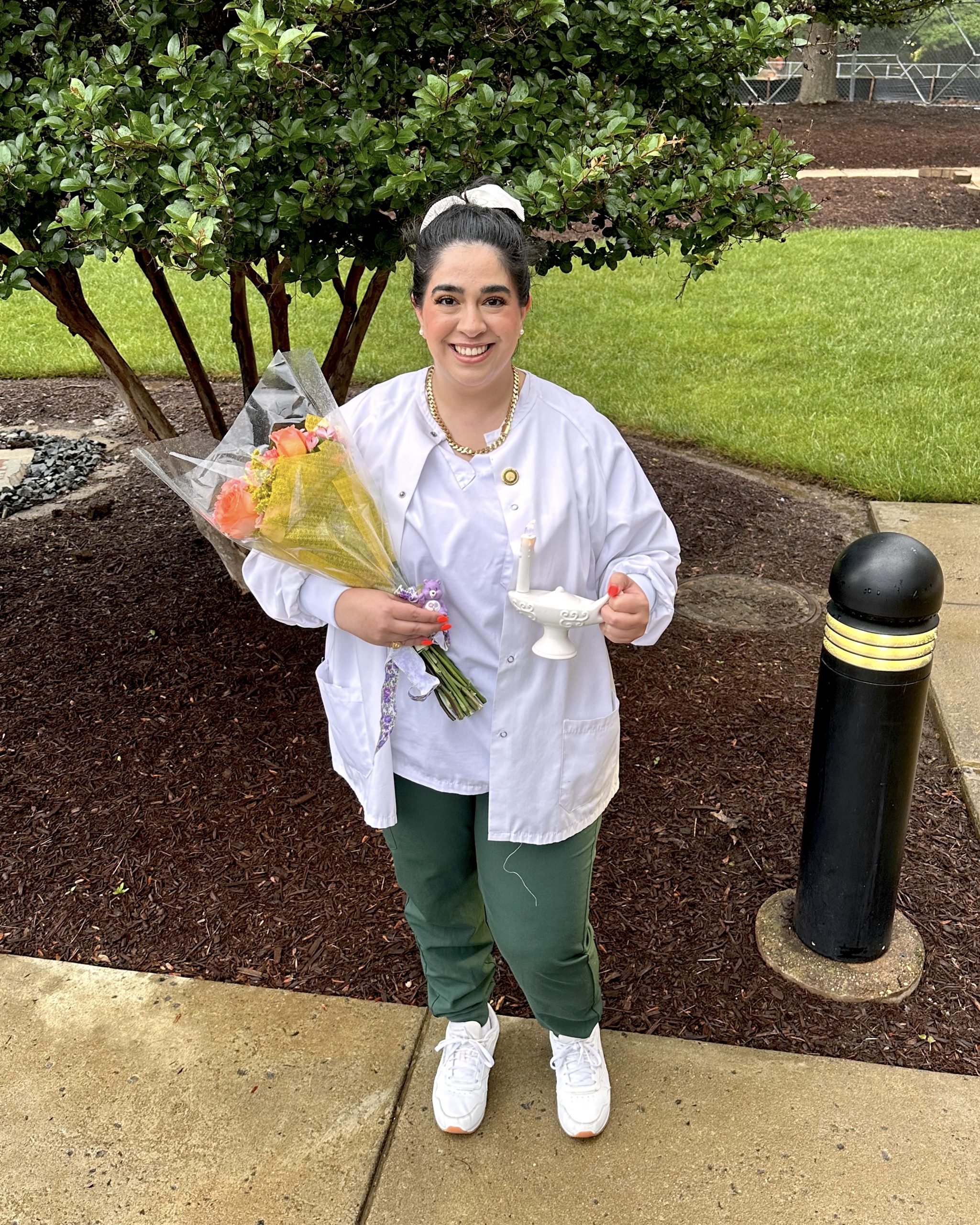 Nour stands outside and holds flowers and a small white lamp symbolizing the lamp of knowledge, the official symbol of the nursing profession and higher education.