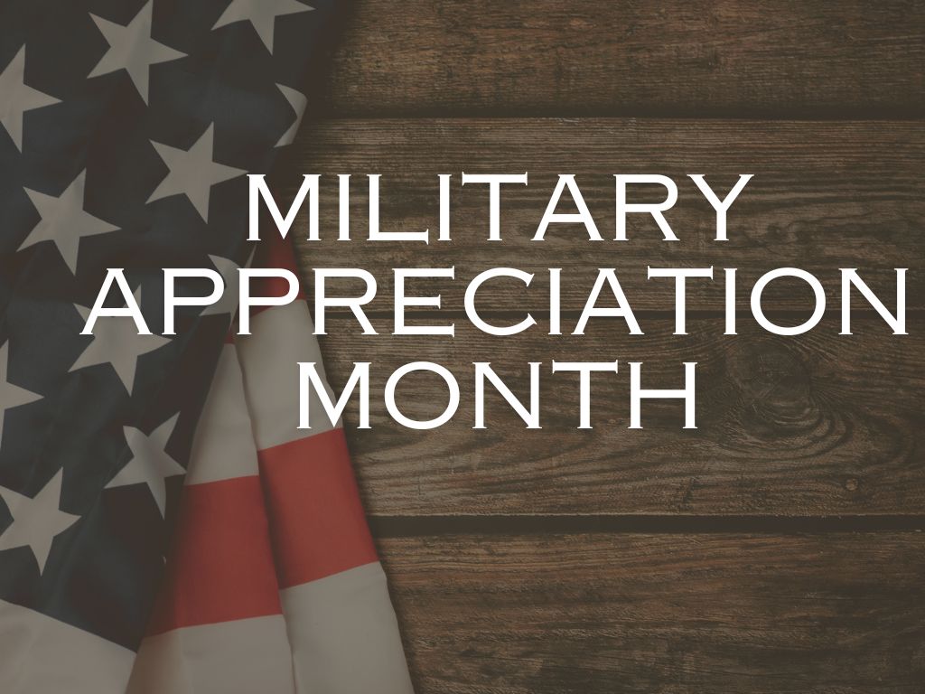 "Military Appreciation Month" appears in white letters against a background resembling dark wood grain with a folded American flag at the left. 