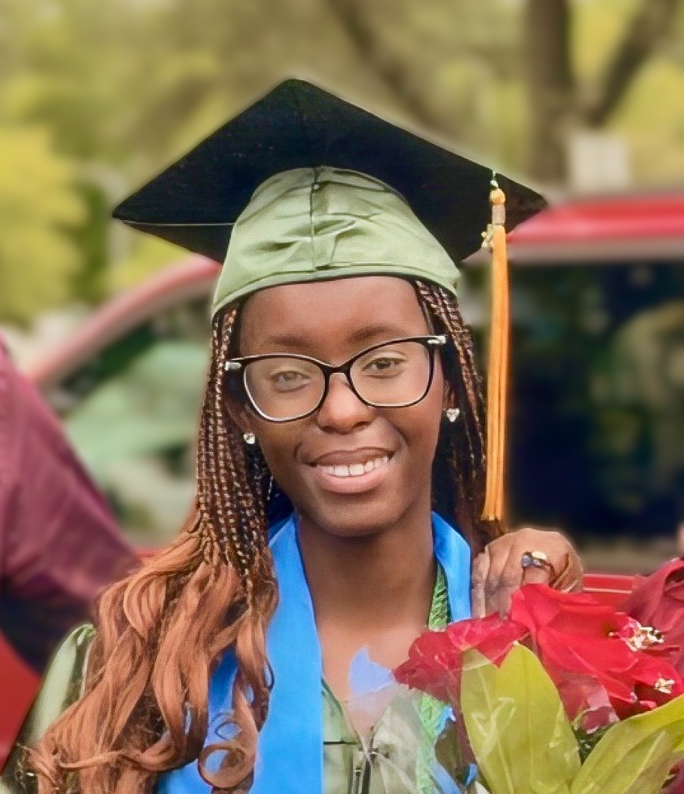 NOVA graduate and soon-to-be George Mason student Bianca Watu, wearing her green cap and gown and a blue stole, smiles for the camera on NOVA's graduation day at George Mason University's EagleBank Arena. Bianca wears dark-rimmed glasses and holds a bouquet of red roses.