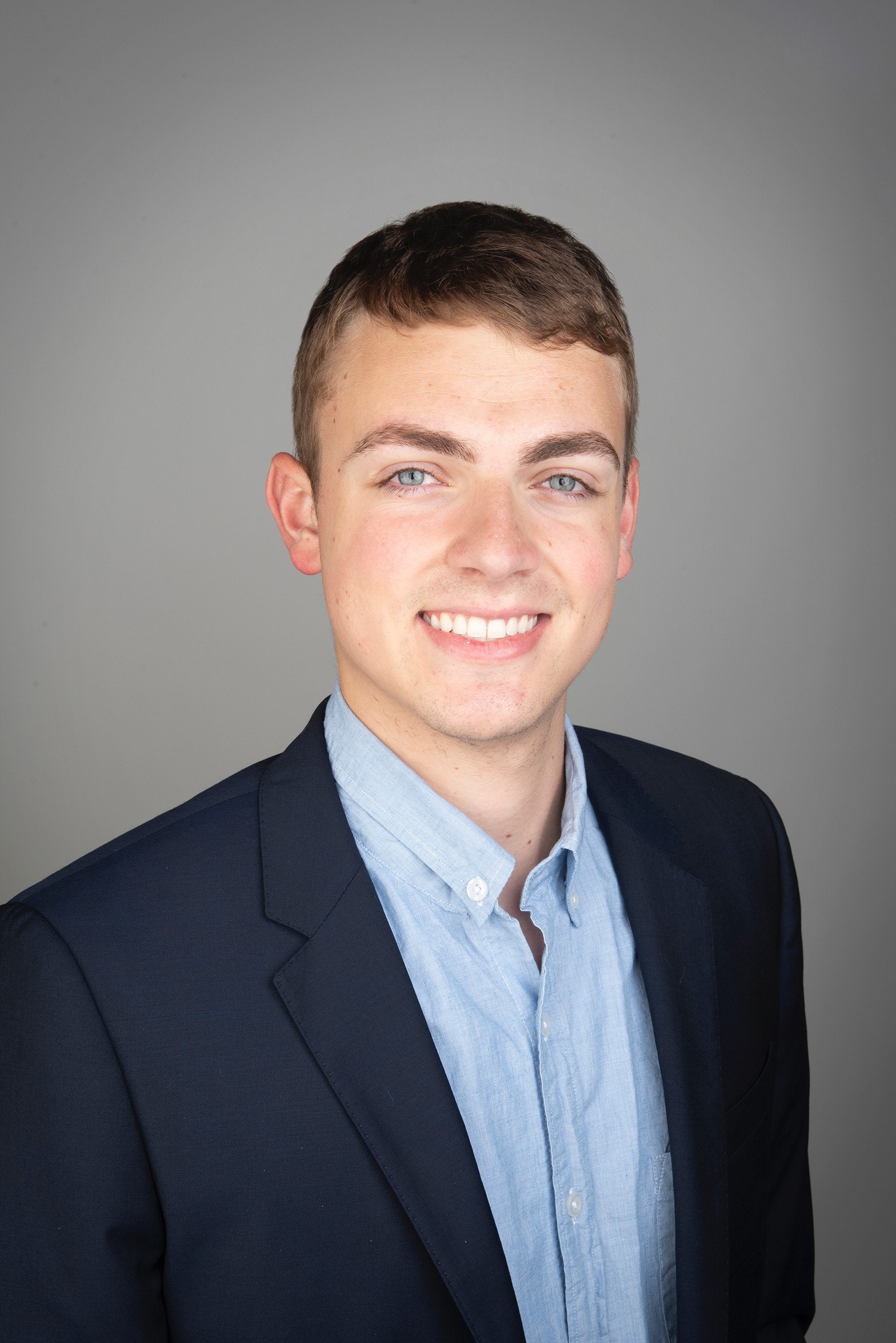 NOVA's Student Support Database Manager Mack Bowen, dressed in a blue Oxford shirt and navy blazer, smiles for the camera in a professional headshot.