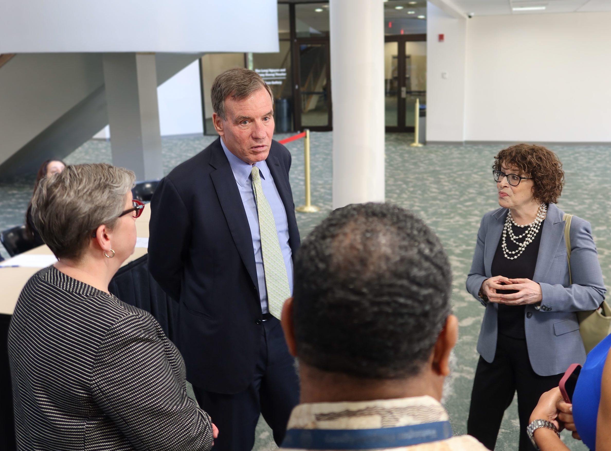 Photograph of NOVA President Anne Kress (left, in a patterned blazer), Senator Mark Warner (center, in a dark suit and yellow tie) and Assistant Secretary of State for Consular Affairs Rena Bitter (right, in a dark blouse and blue jacket) as they at last month's Passport Day event on the Annandale Campus.