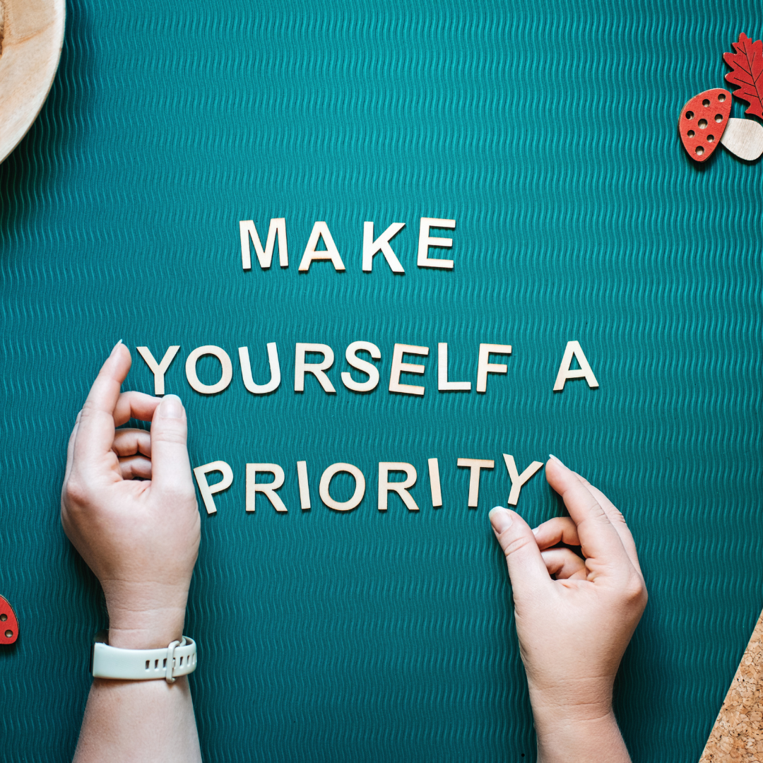 Teal colored bulletin board with red and white foam mushrooms and two hands placing letters that say, "May Yourself a Priority."