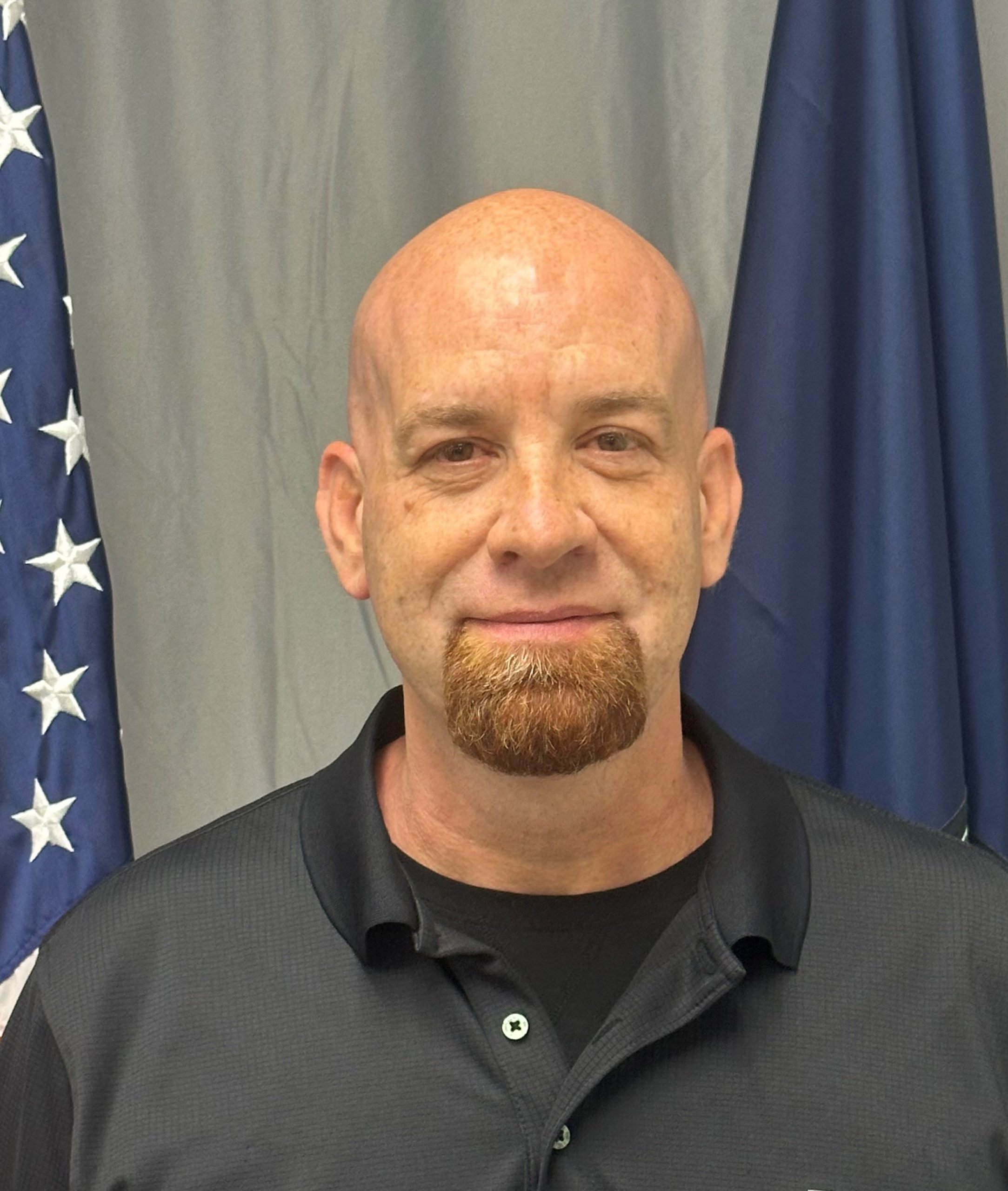 Dave Cook poses before a grey screen and an American flag and a Virginia flag