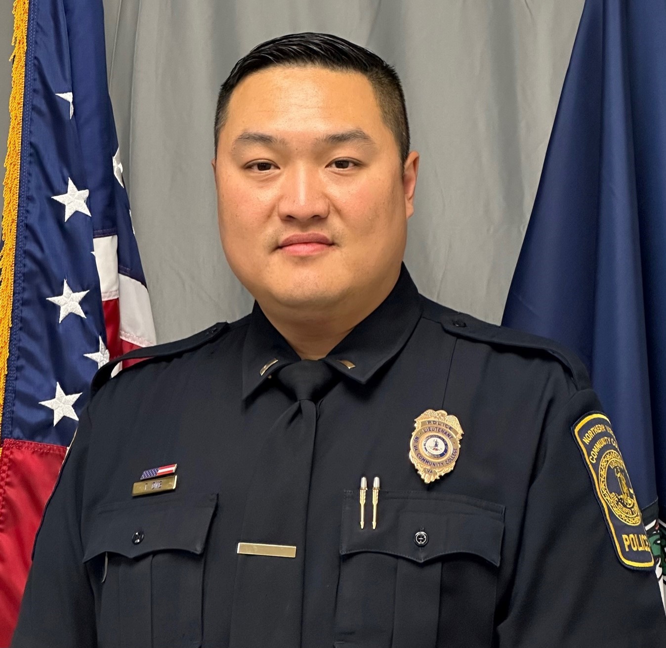 Professional portrait of Lieutenant Ong with a grey curtain backdrop and an American flag and a Virginia flag.
