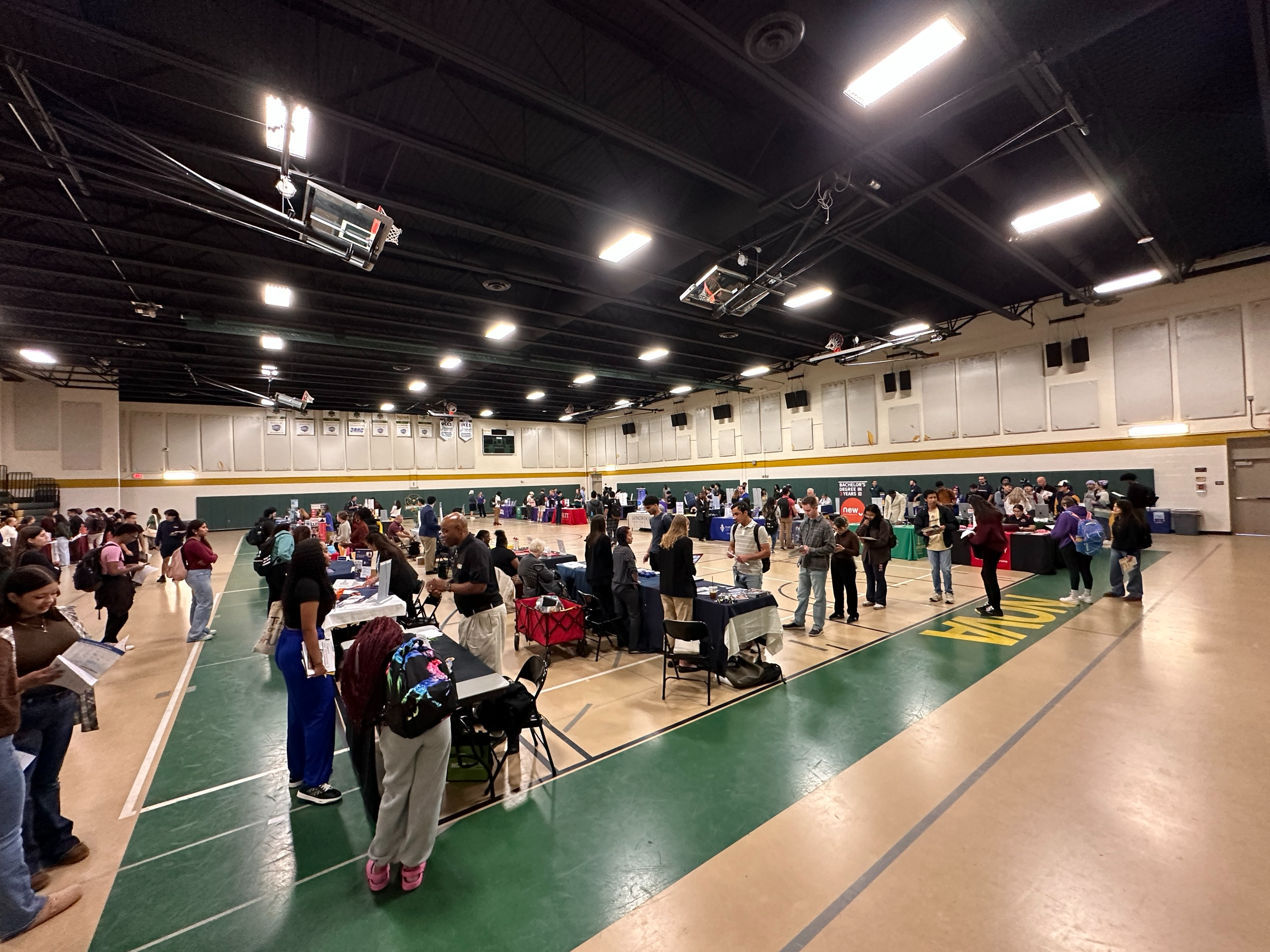Students wander the aisles between tables at a college transfer fair set up in the Ernst Center gym.