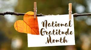 A little note that says National Gratitude Month attached to a tree limb with clothespins and a colorful fall leaf