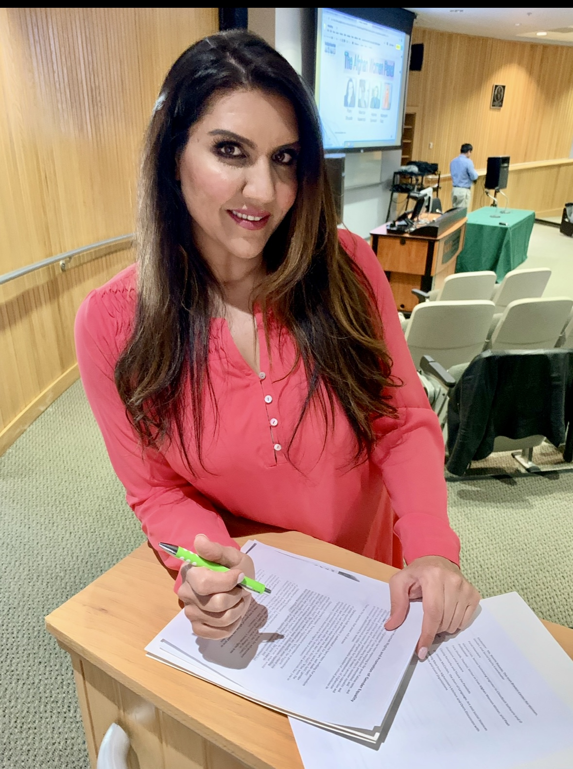 Sophia Sexton smiles as she stands in a lecture hall making notes on a paper.
